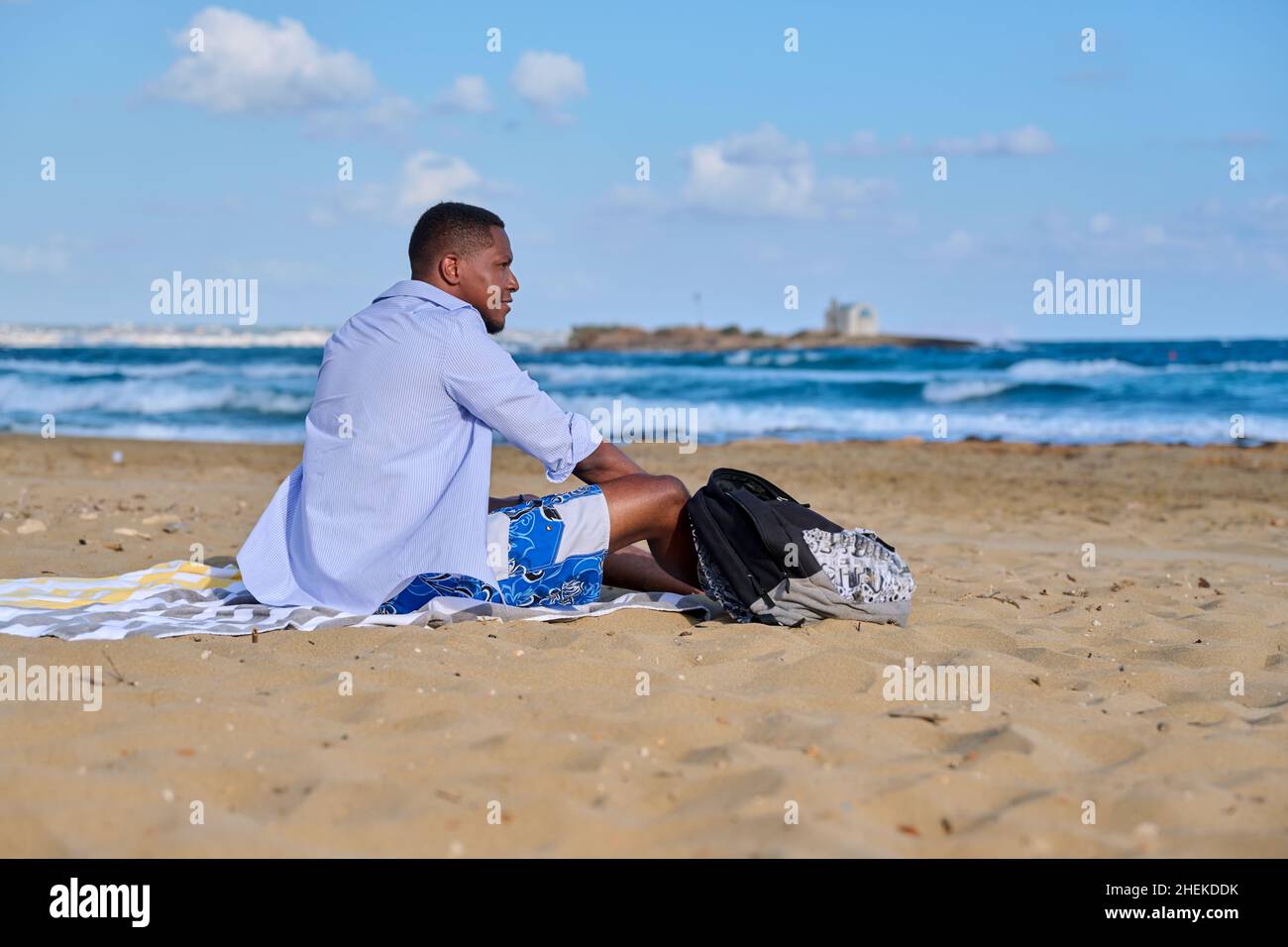 Young positive male tourist sitting resting on the beach Stock Photo