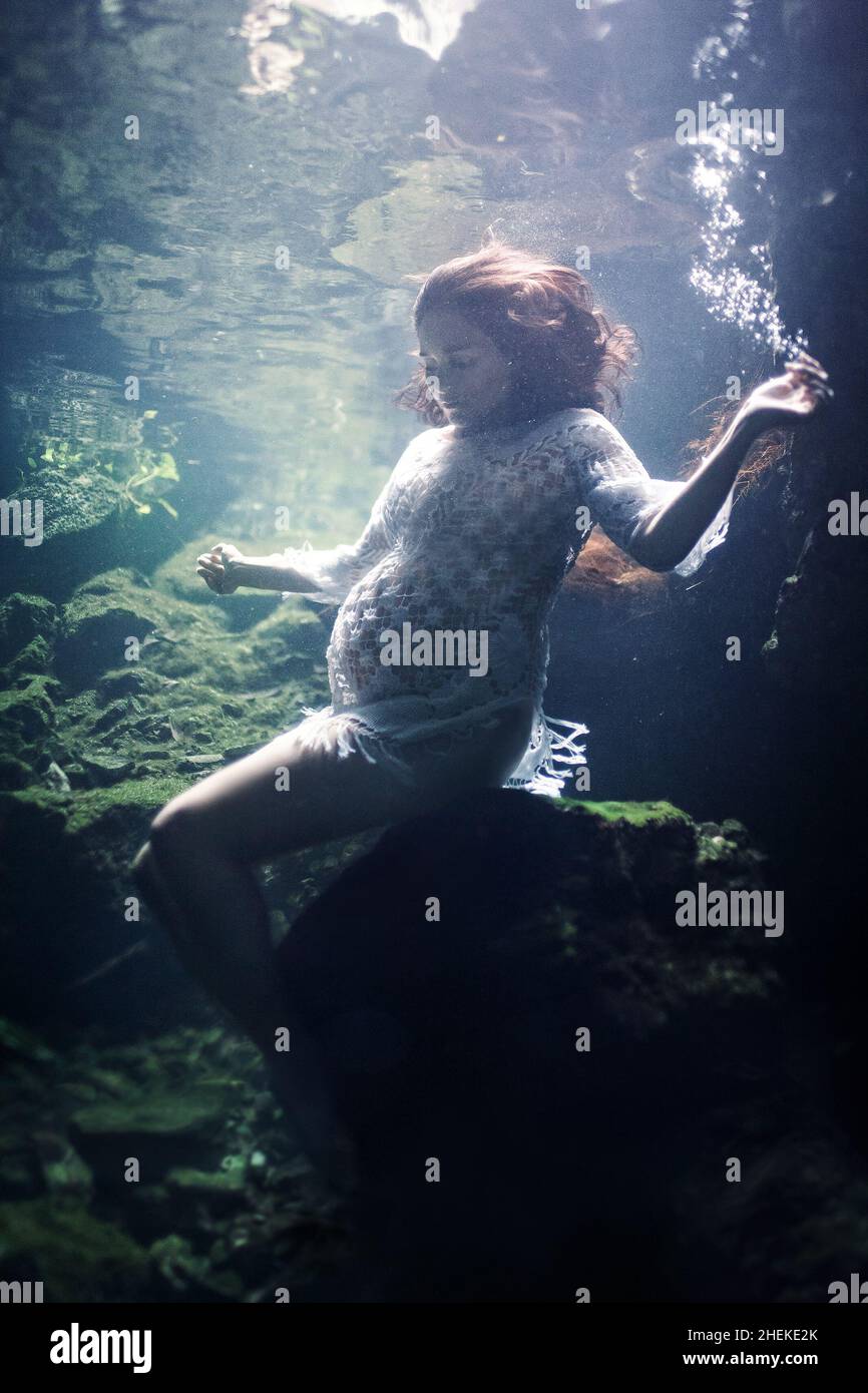 Young pregnant woman in an underwater cave in a white dress Stock Photo