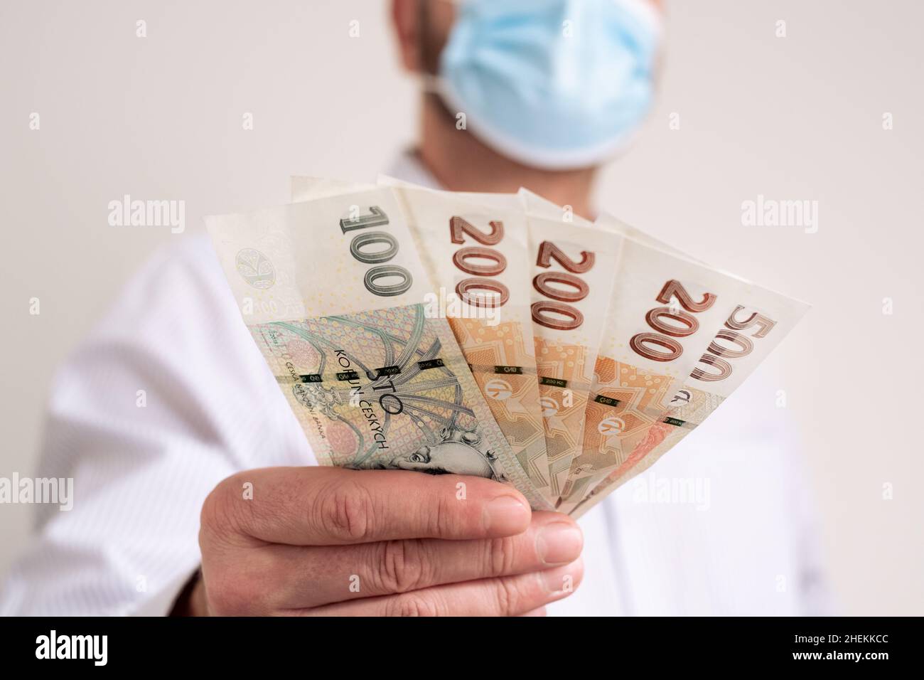 Fan of Cash Czech republic koruna. Finance during coronavirus in Czechia concept. CZK small banknotes. Man in a protective medical face mask holds kro Stock Photo