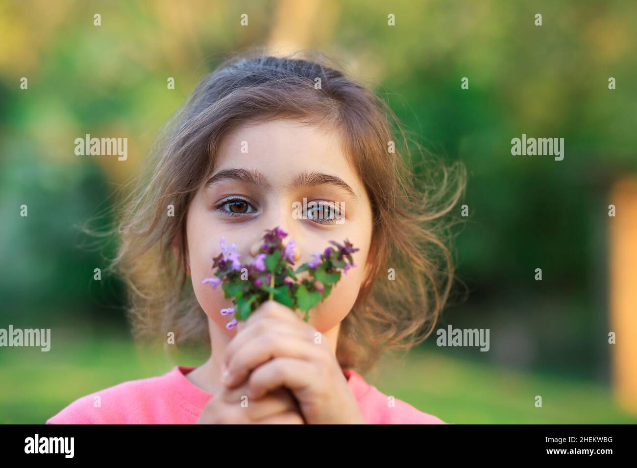 Little cute girl with pinc flowers. Child  playing in summer garden. Kids gardening. Children play outdoors. Toddler kid with flower bouquet for birth Stock Photo