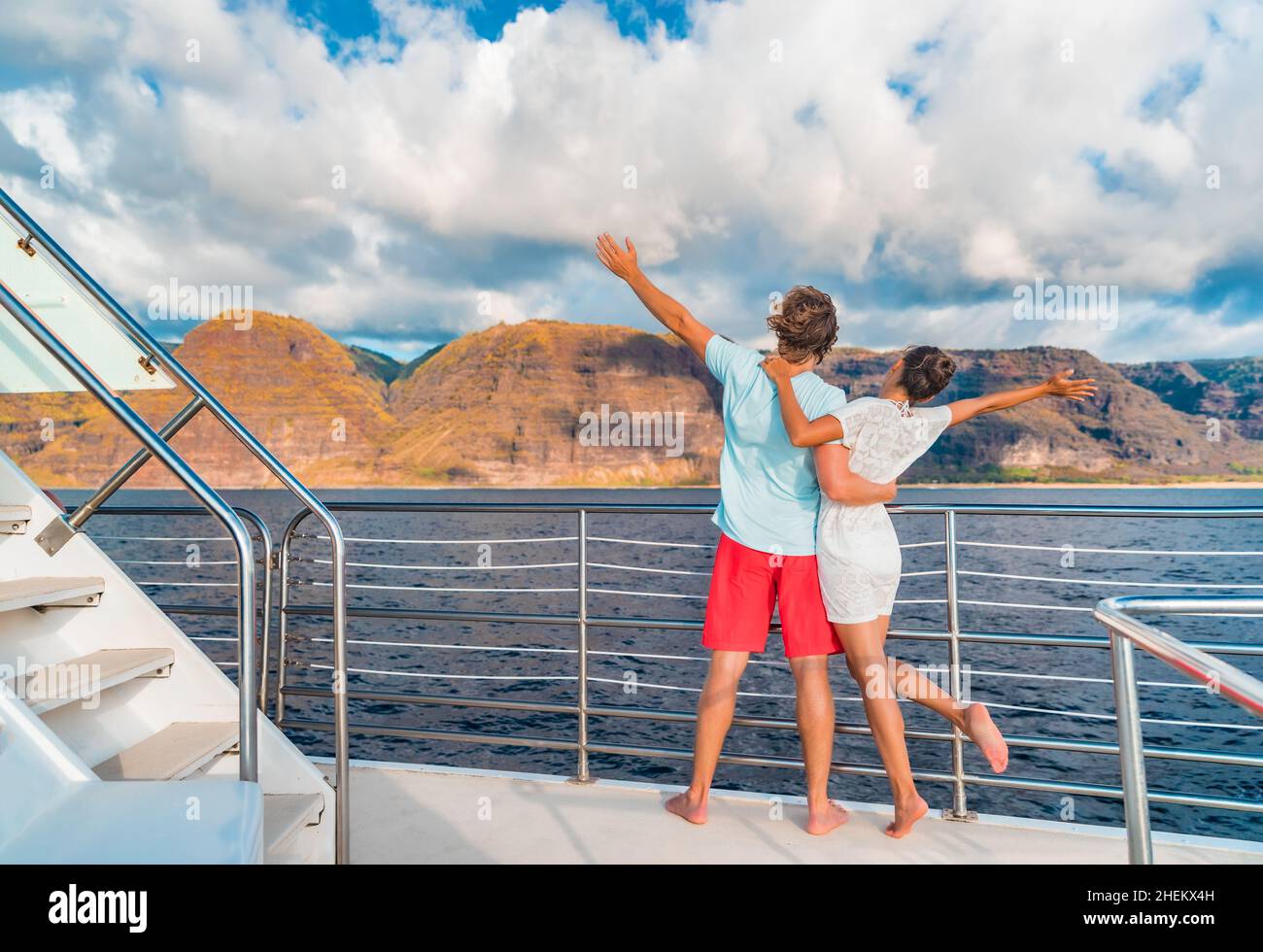 Couple on luxury yacht cruise ship tour at sunset feeling free happy with open arms in fun looking at mountain scenery. Romantic sunset boat ride Stock Photo