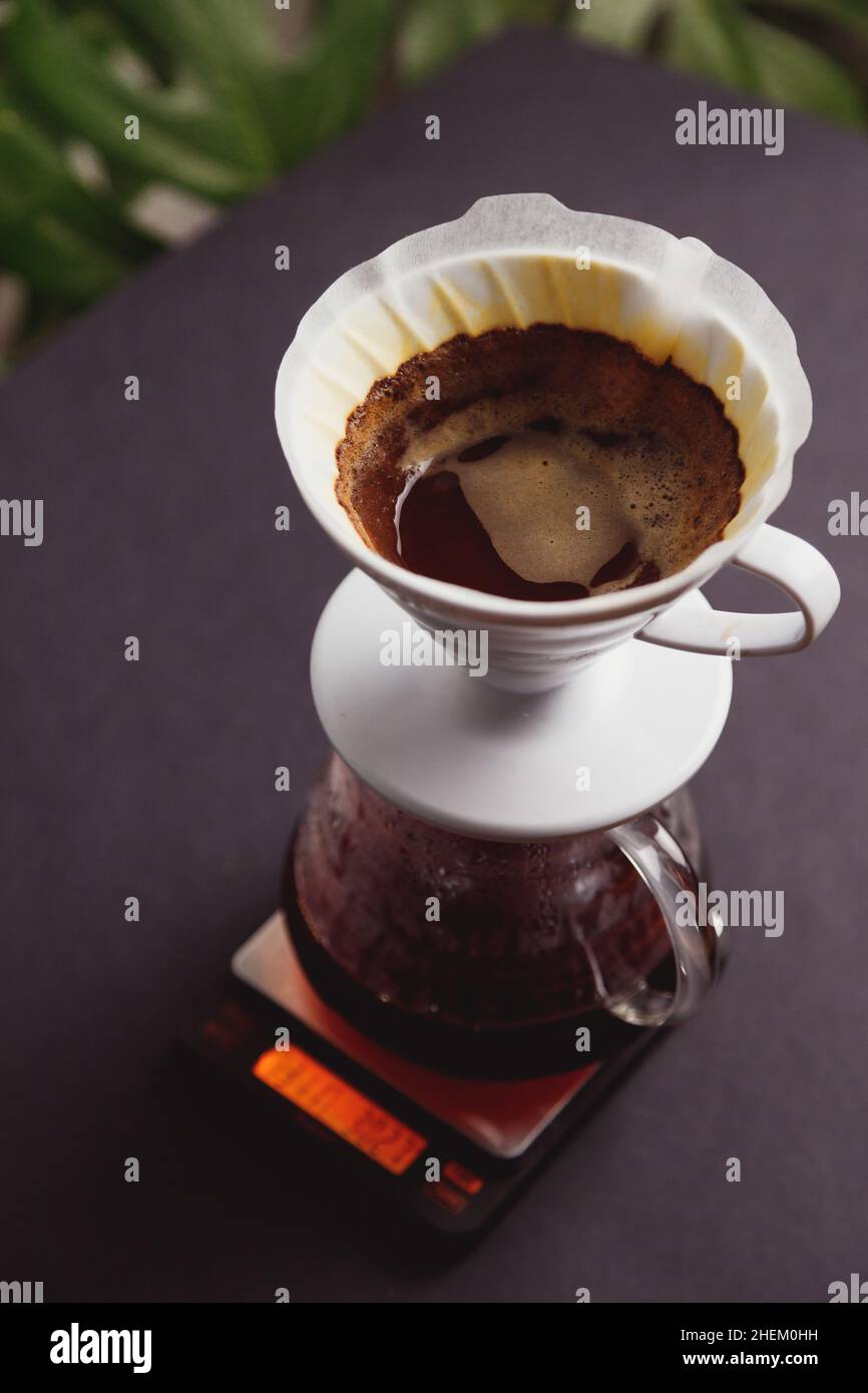Brewing ground coffee through paper filters into a glass coffee pot. Standing on electronic scales Stock Photo