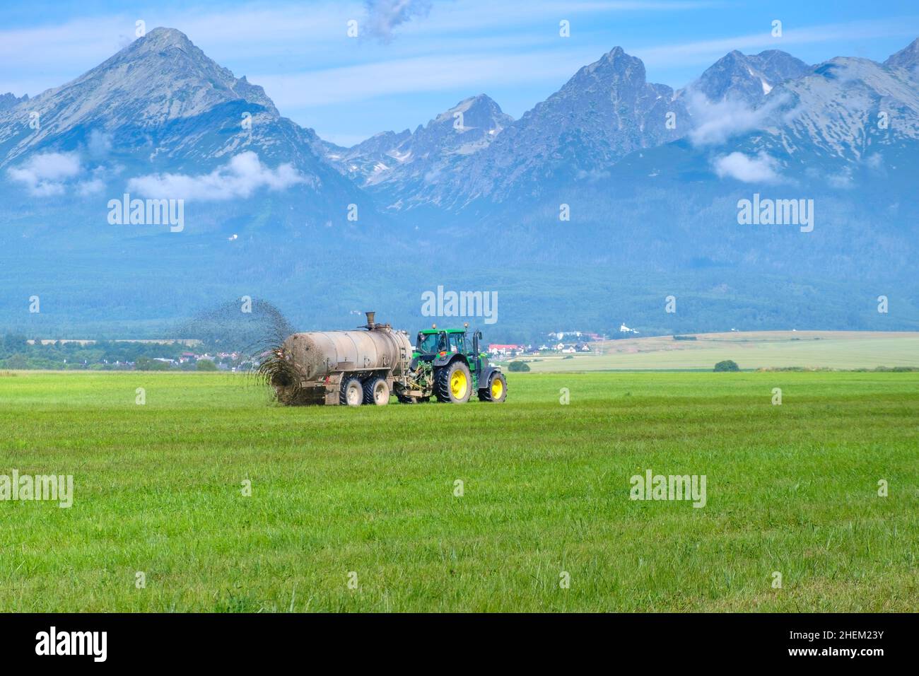 A big tractor spreading fertilizer to improve the harvest on pasture meadow or field in the High Tatra mountains. Landfarming concept . Stock Photo