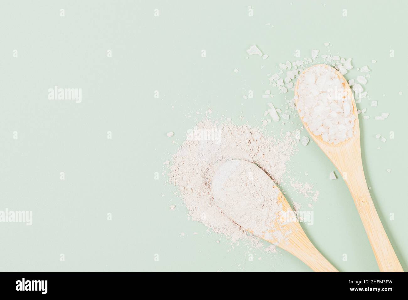 Cosmetic clay and sea salt in wooden spoons ingredients for homemade beauty treatments on green background with copy space, flat lay Stock Photo
