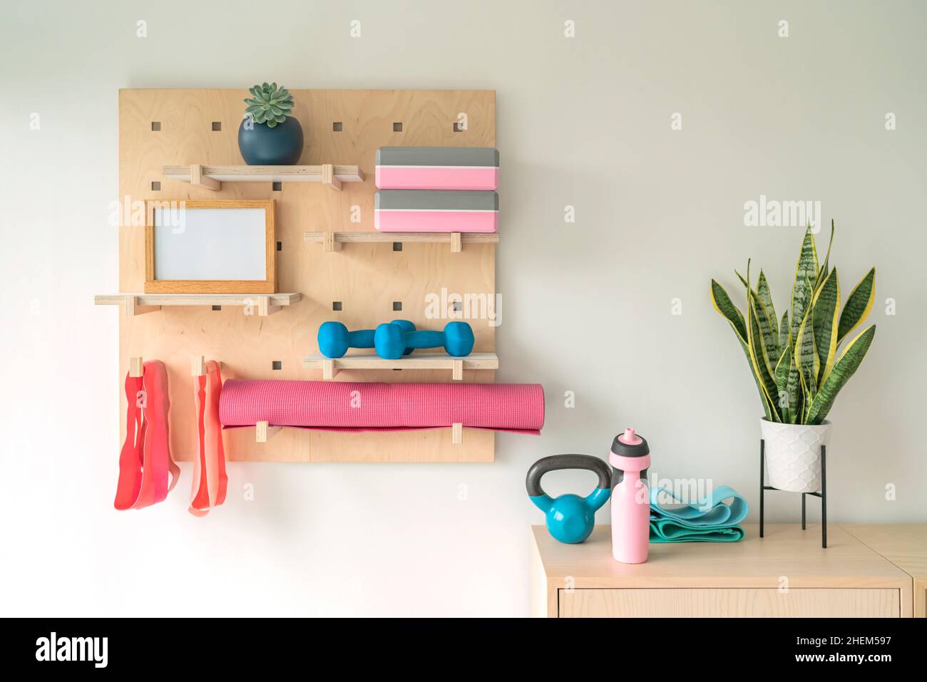 Workout fitness at home gym organized shelves for pilates equipment. Wood pegboard storing resistance bands, weights, yoga blocks, motivational Stock Photo