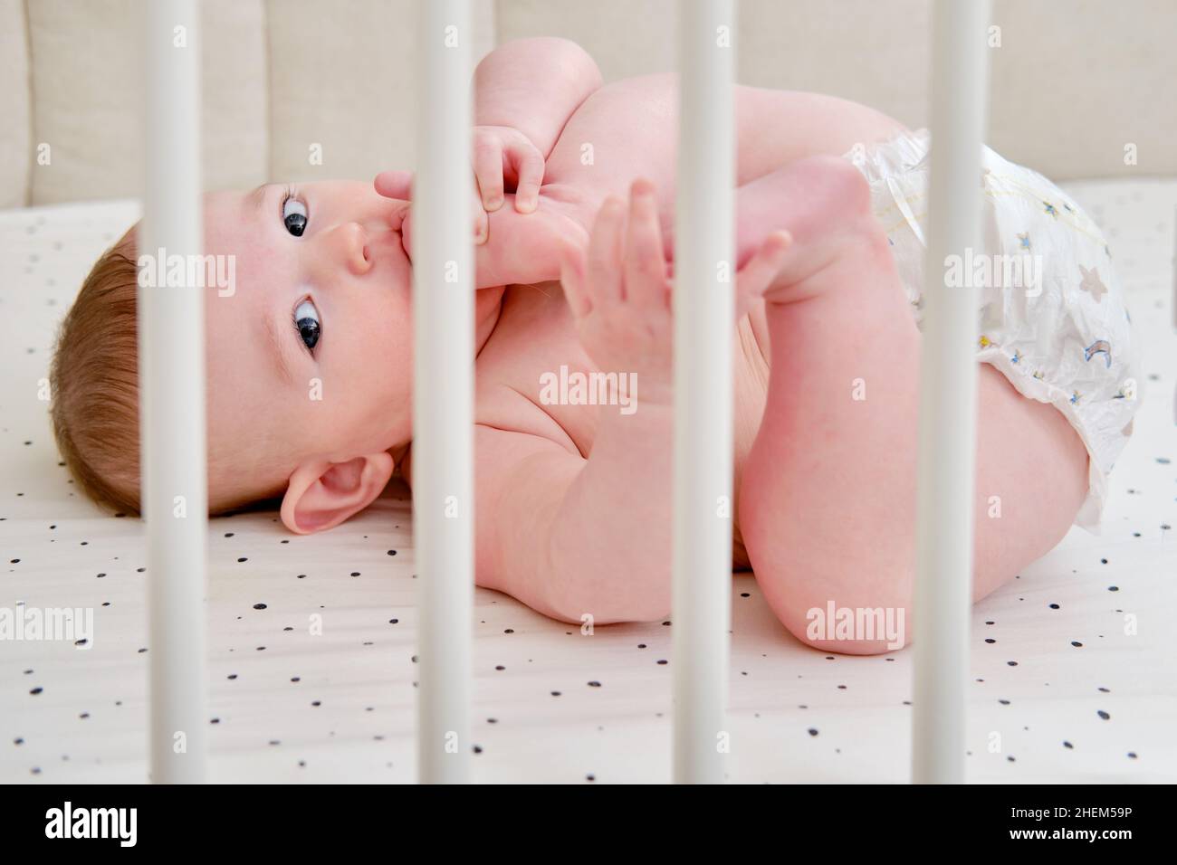 A happy infant baby with teething teeth in a diaper pulls his hand into