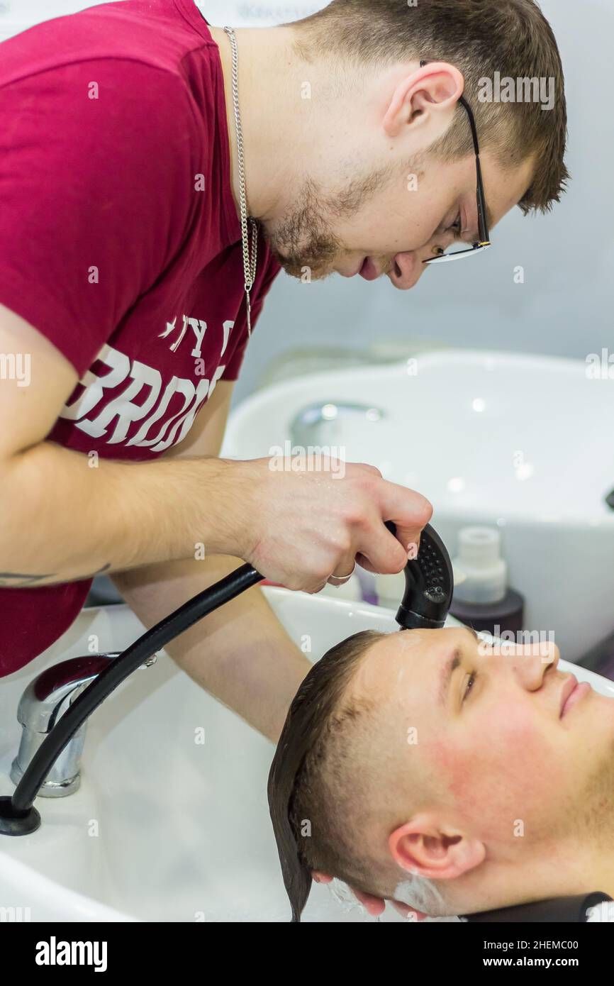 Male hairdresser rinsing shampoo from client's hair in salon. Russia Moscow 17 November 2016. Stock Photo