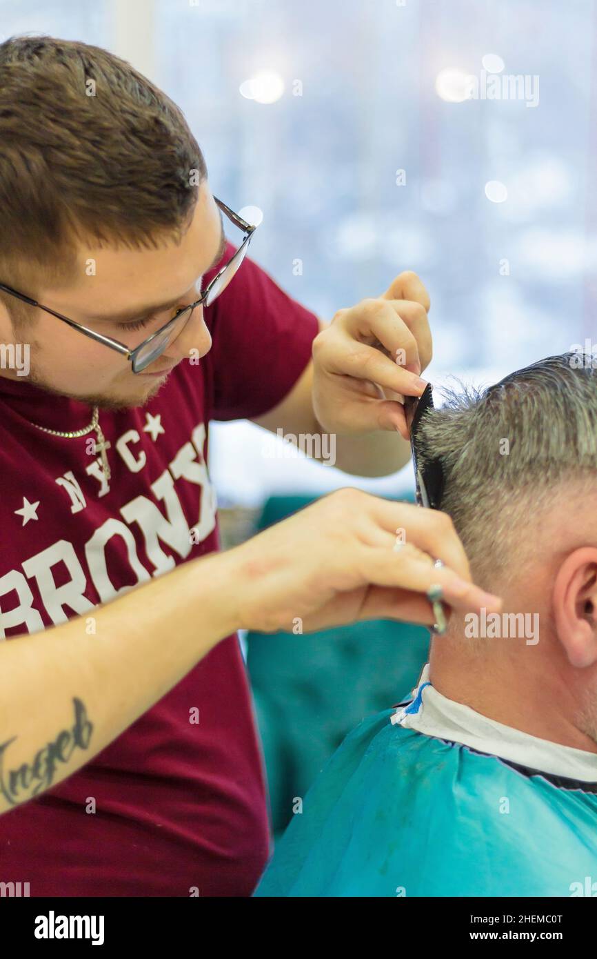 A male hairdresser makes a haircut for a client with scissors and a comb. The man had his hair cut at the barbershop. Russia Moscow 17 November 2016. Stock Photo
