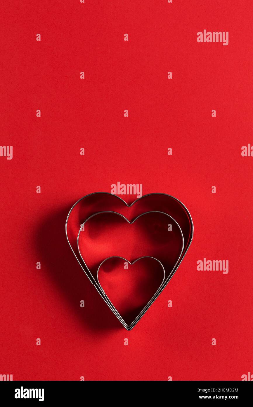Saint Valentine day minimalistic greeting card, heart-shaped cookie cutters on red background with beautiful shadows, flat lay Stock Photo