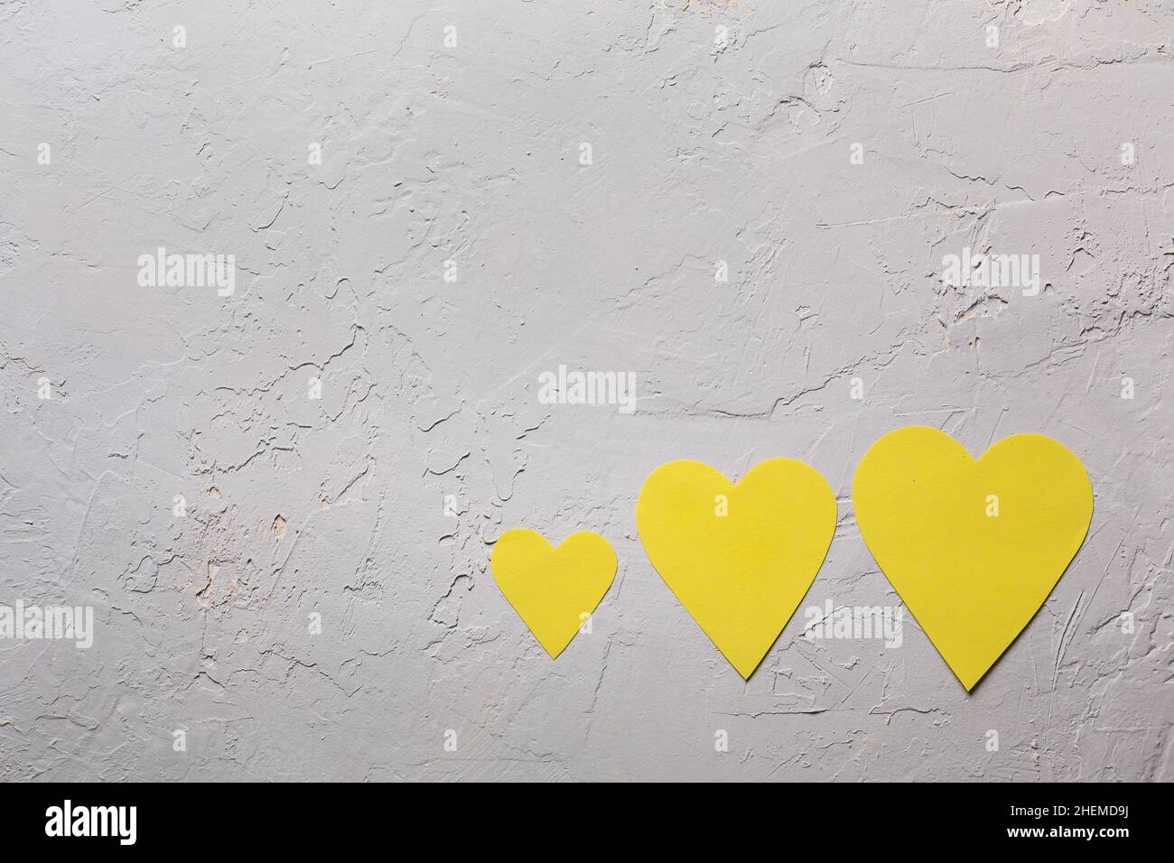 Saint Valentine day minimalistic greeting card in ultimate grey and illuminate yellow colors of the 2021 year, three paper hearts on textured backgrou Stock Photo