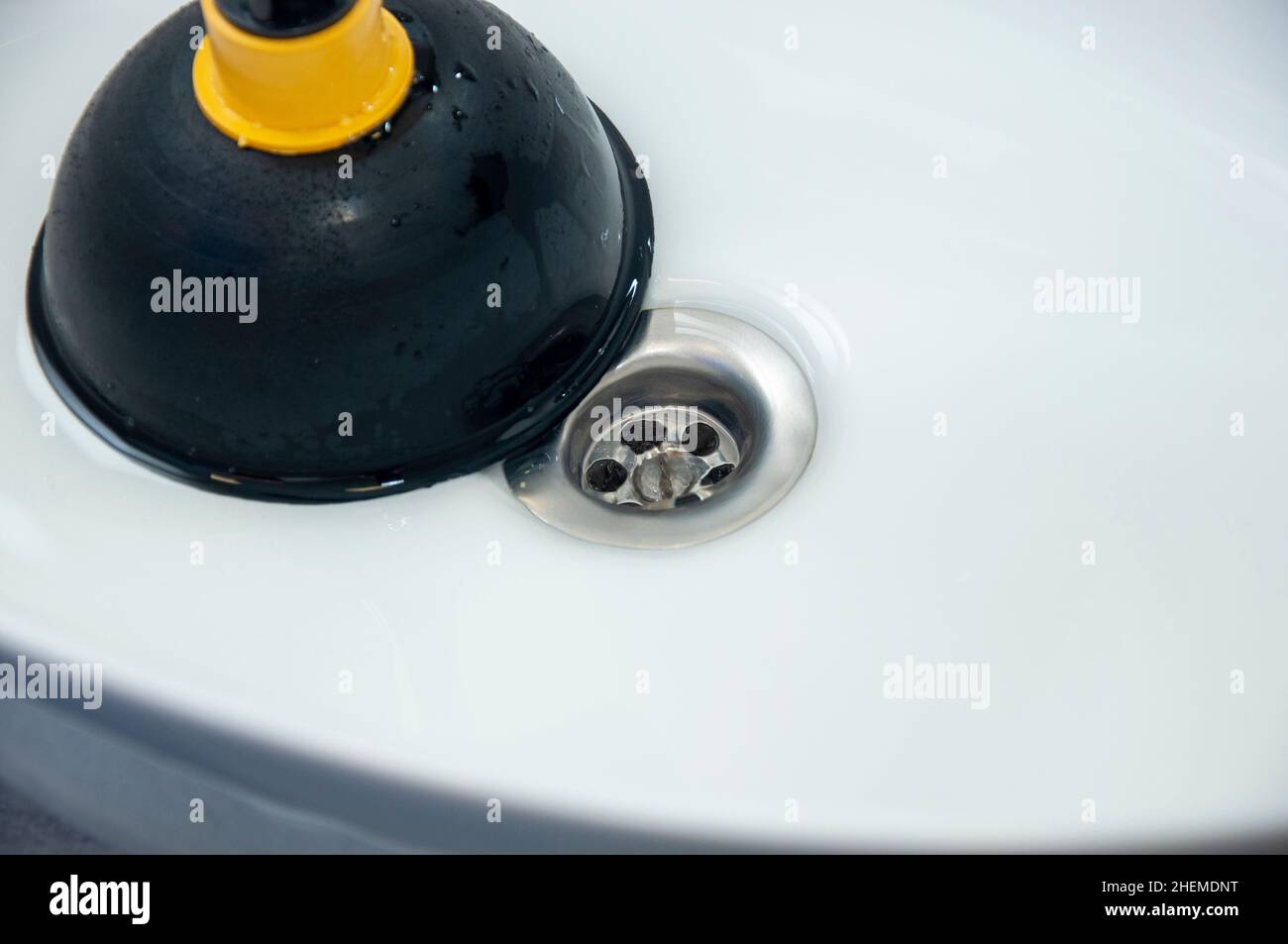 Cleaning sink with plunger in bathroom. Concept of plumbing problem and