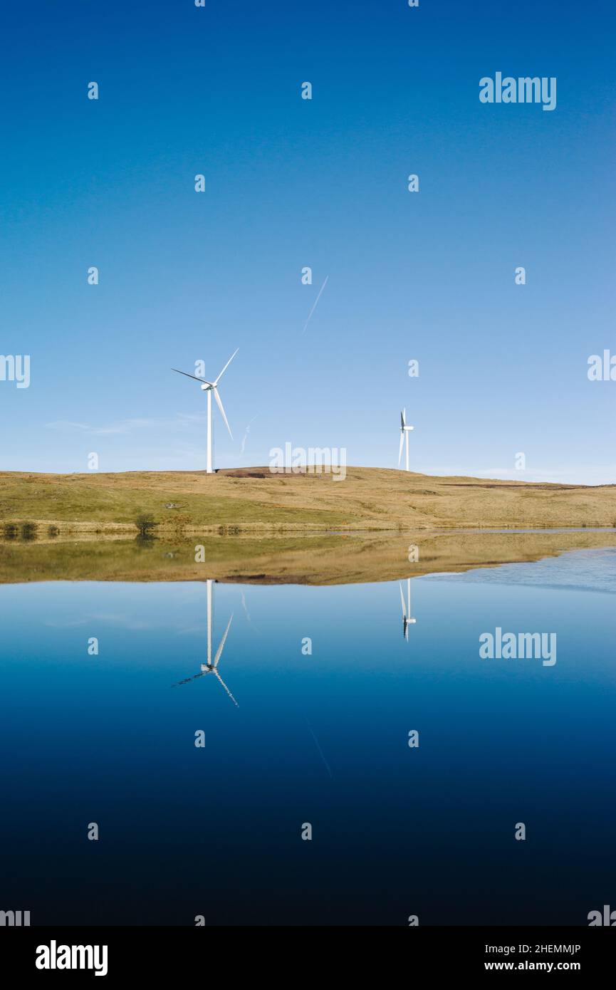 Two wind turbines reflected in a small lake or loch on a sunny day with a blue sky. Stock Photo