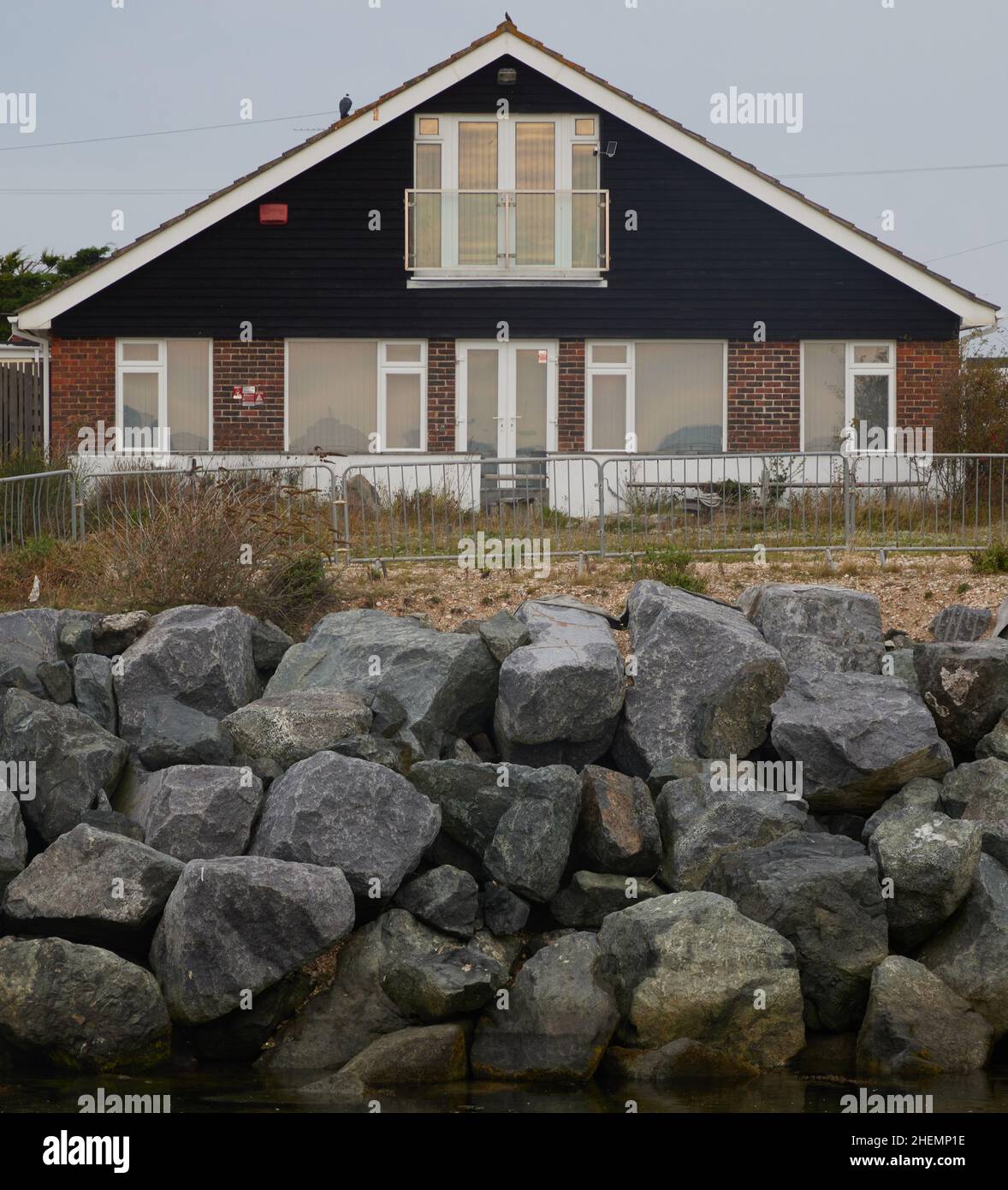 House seen protected  against coastal erosion with large rocks on Pagham beach. Stock Photo