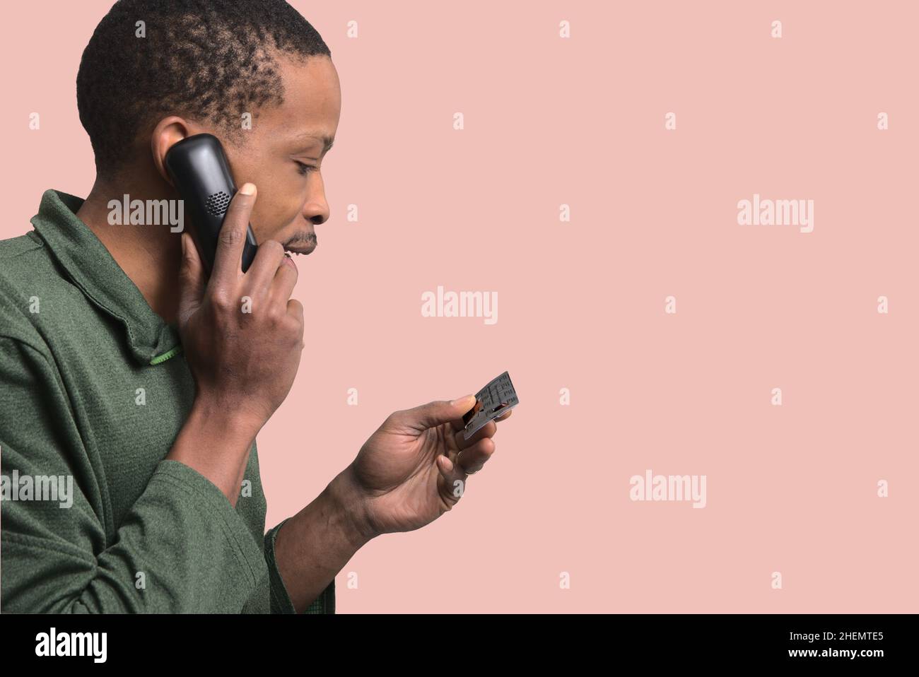 young man talking on the phone and reading a card in his hand on a plain background Stock Photo