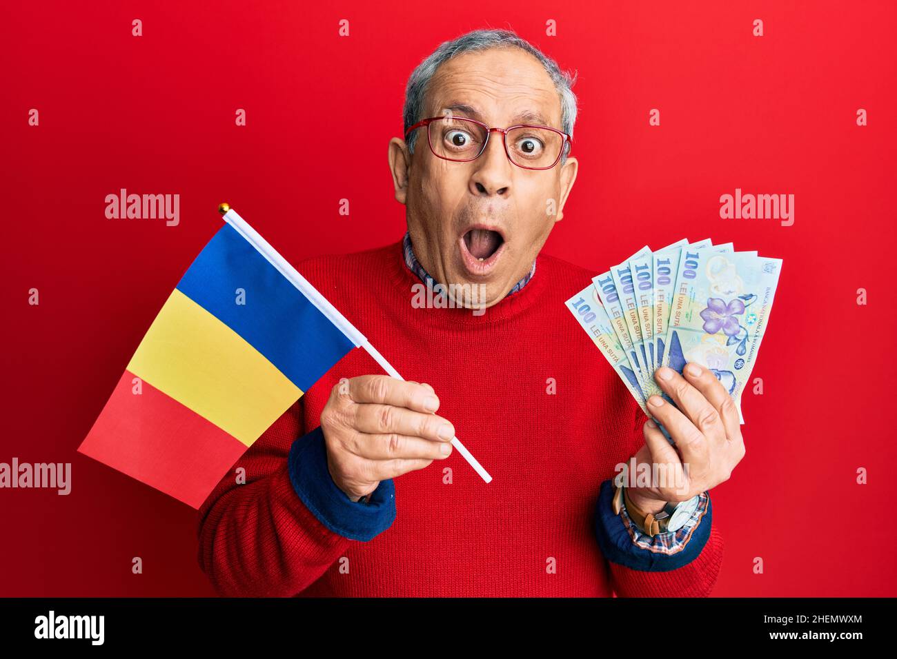 Handsome senior man with grey hair holding romania flag and leu banknotes afraid and shocked with surprise and amazed expression, fear and excited fac Stock Photo
