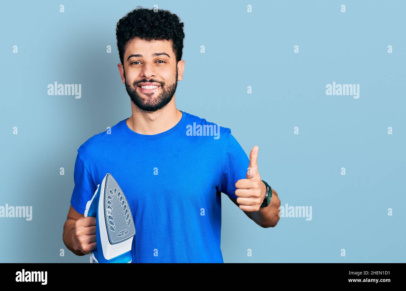 Young arab man with beard holding electric steam iron smiling happy and