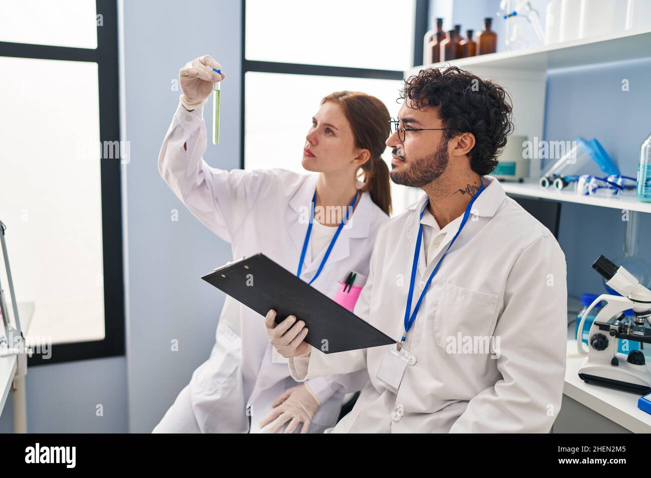Man and woman scientist partners looking test tube holding clipboard at ...