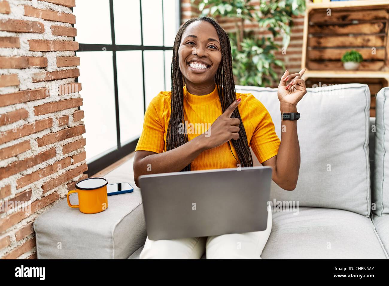 African woman sitting on the sofa using laptop at home smiling and ...