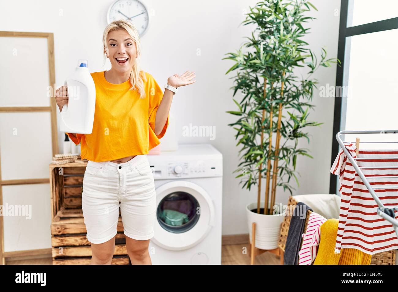 Young caucasian woman doing laundry holding detergent bottle ...