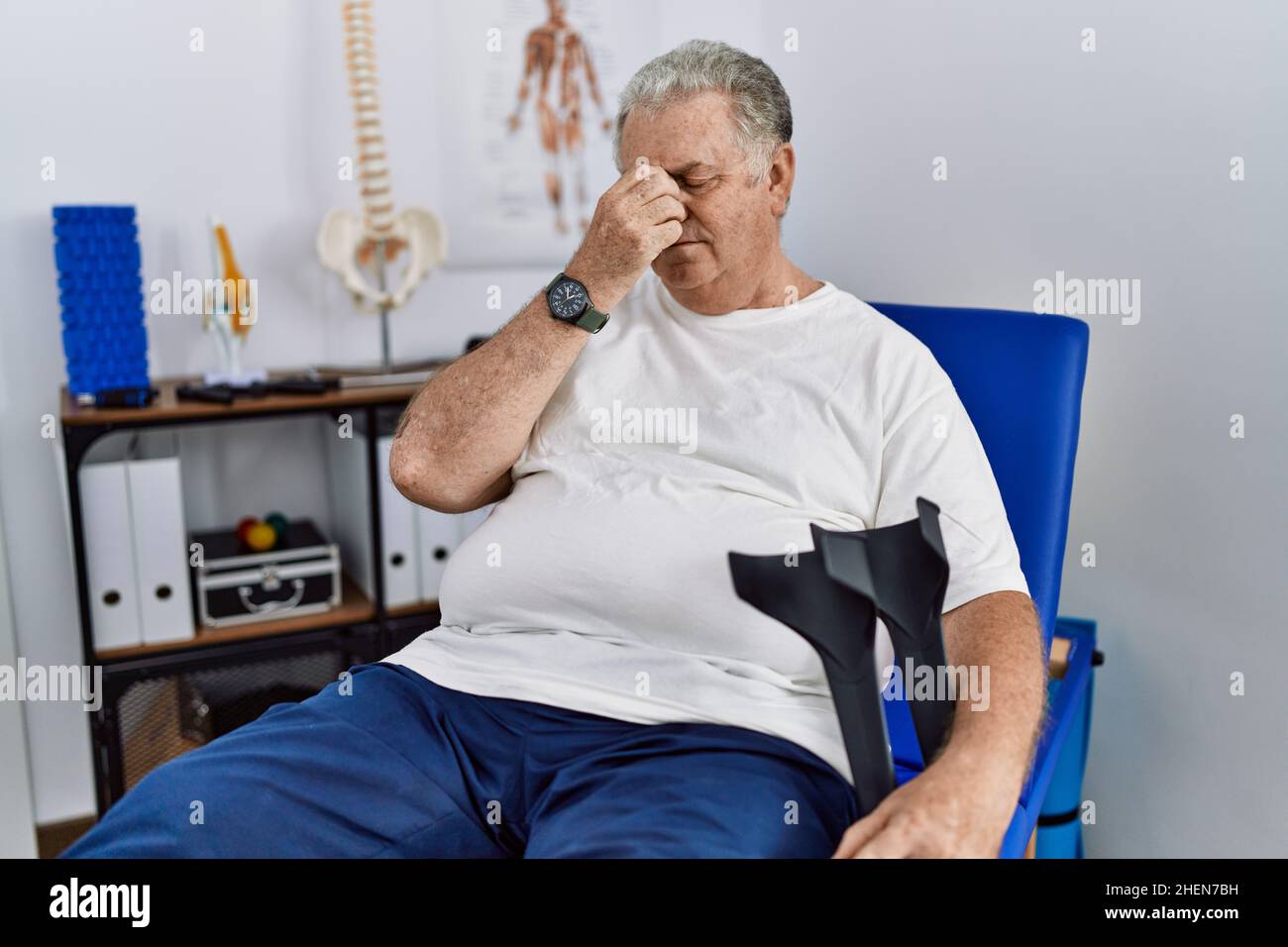 Senior caucasian man at physiotherapy clinic holding crutches tired
