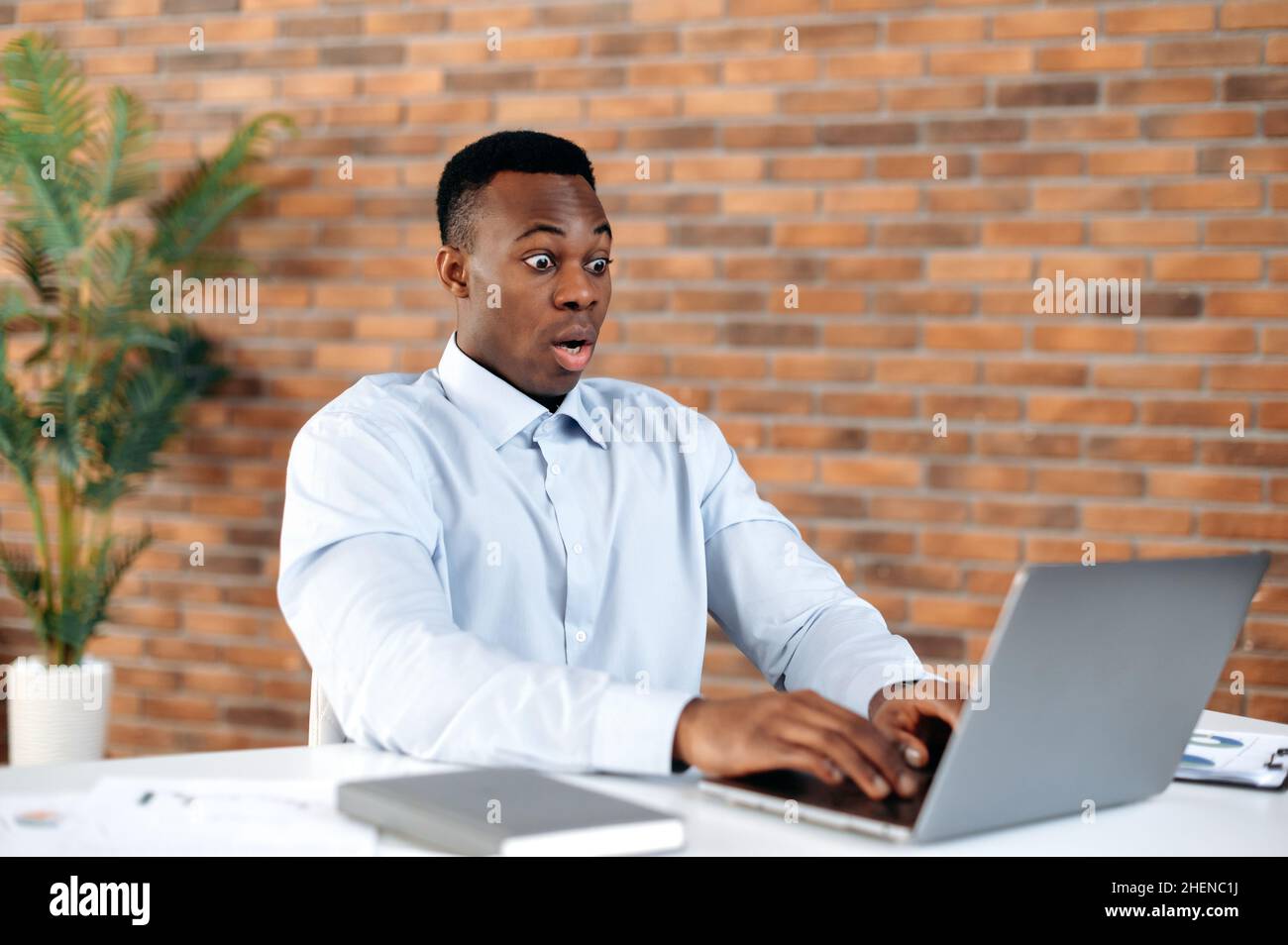 Get unexpected news. African american black shocked man, office employee, CEO, looking in surprise at the laptop screen on modern office, received an unexpected message, amazed facial expression Stock Photo