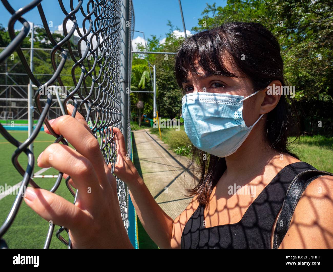 Young Brunette Woman Using a Blue Mask is Looking Through the Mesh of the Soccer Field Stock Photo
