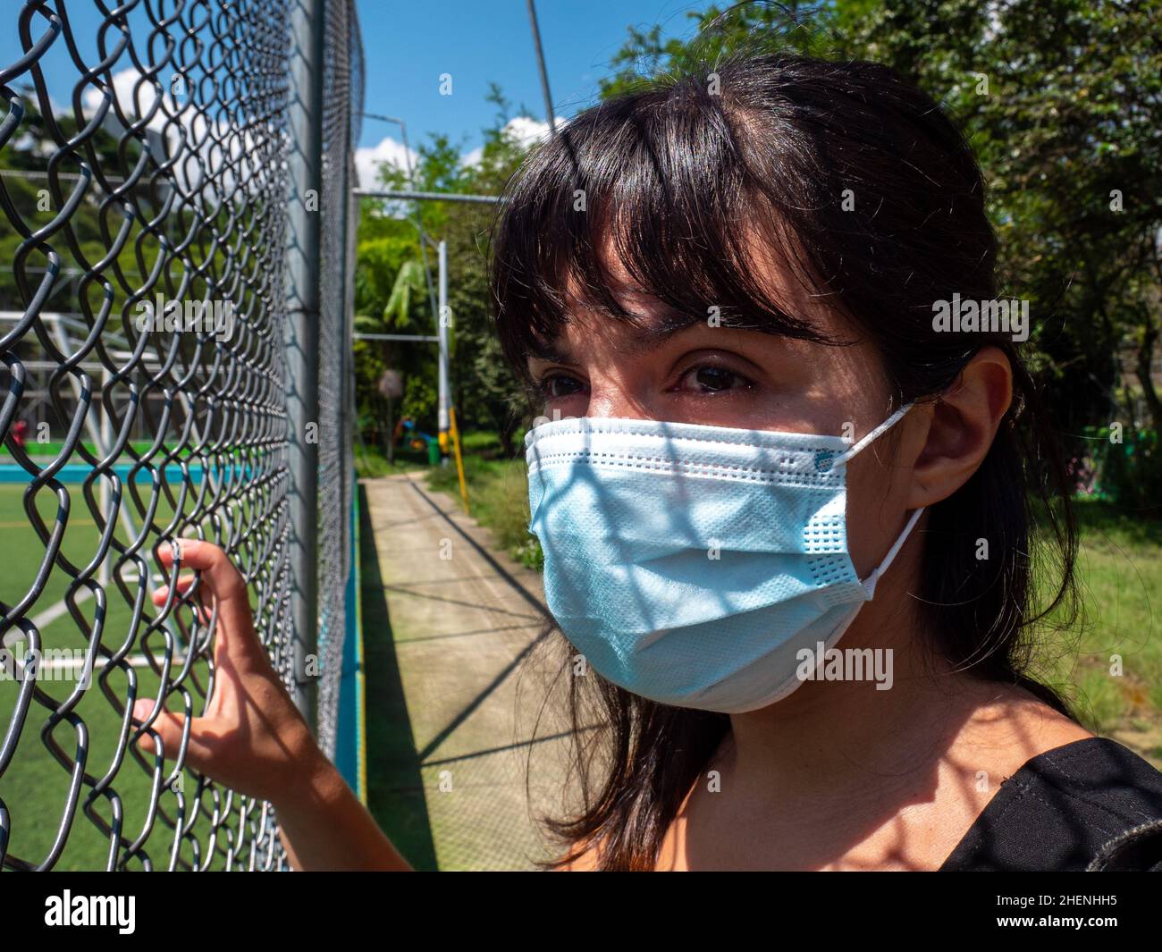 Young Brunette Woman Using a Blue Mask is Looking Through the Mesh of the Soccer Field Stock Photo