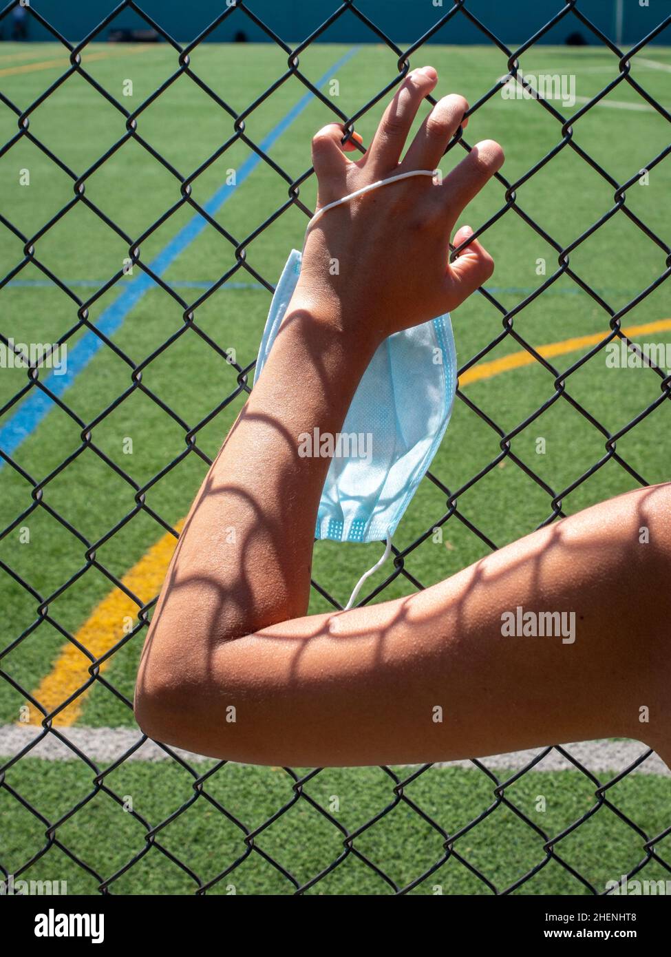 Young Brunette Woman Holding a Mask is Looking Through the Mesh of the Soccer Field Stock Photo