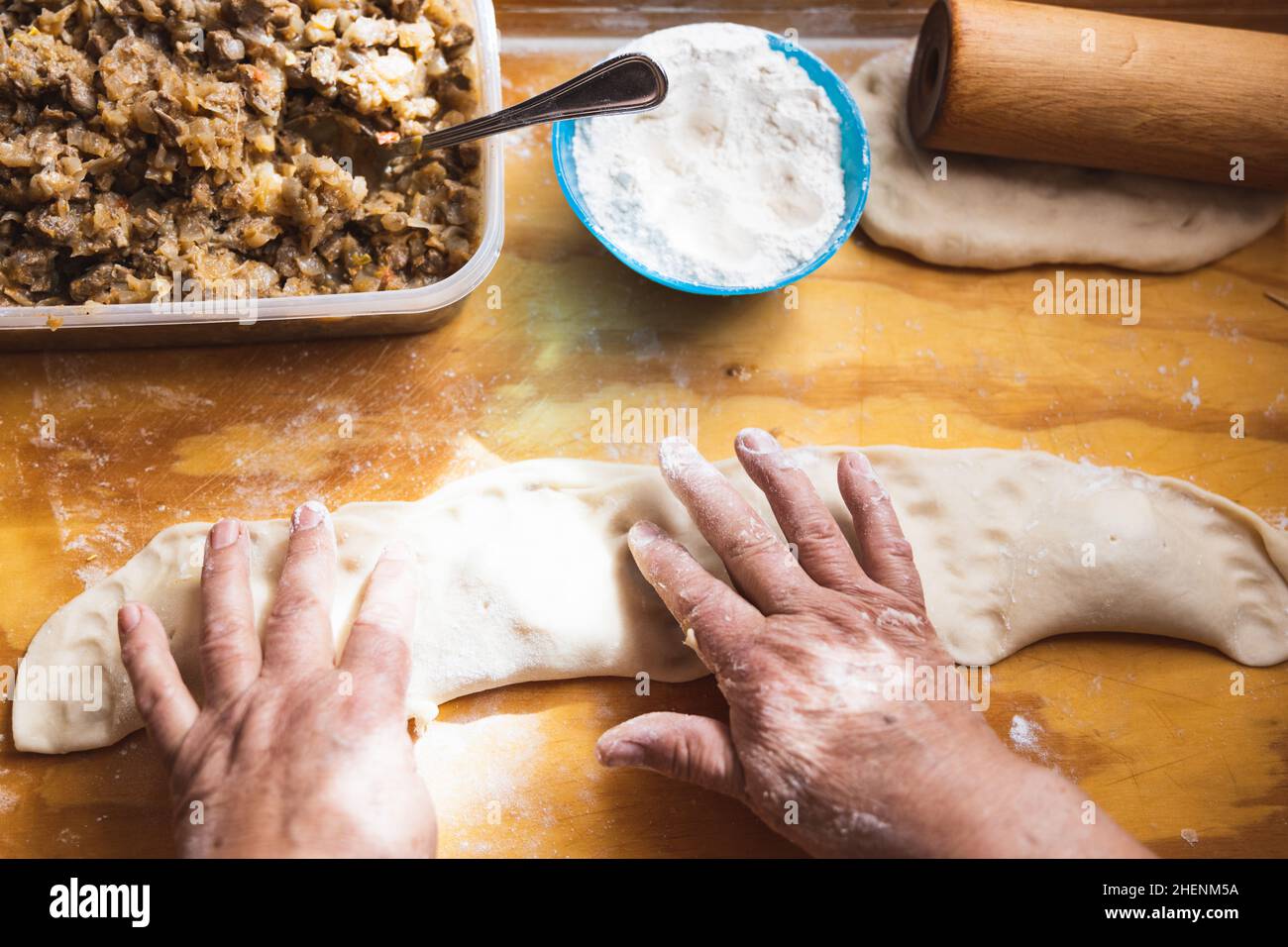 Old woman's hands kneading bread dough. Empanadas. Wooden table. Stock Photo