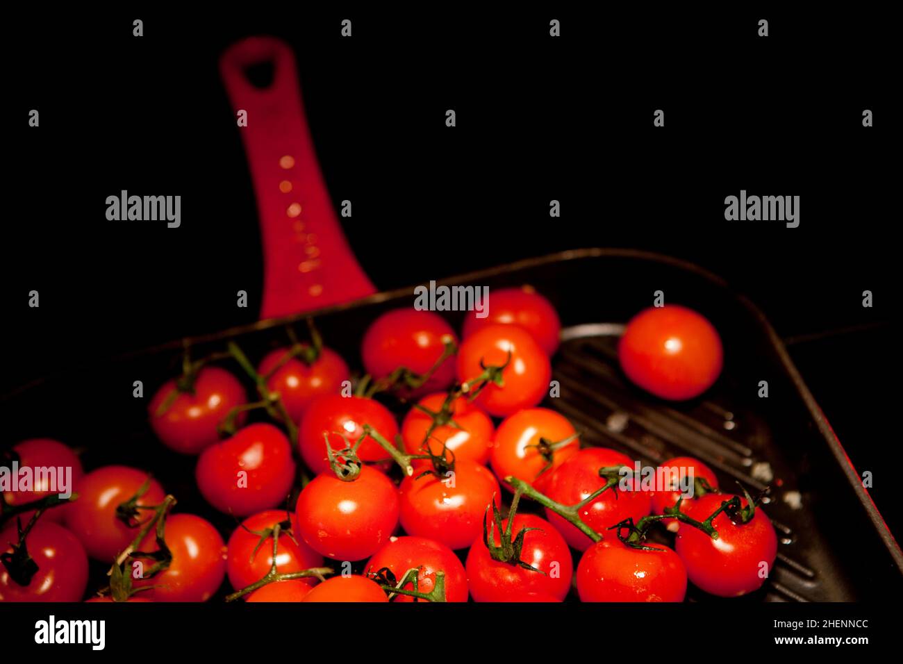 Ripe cherry tomatoes on a red-handled griddle. Stock Photo