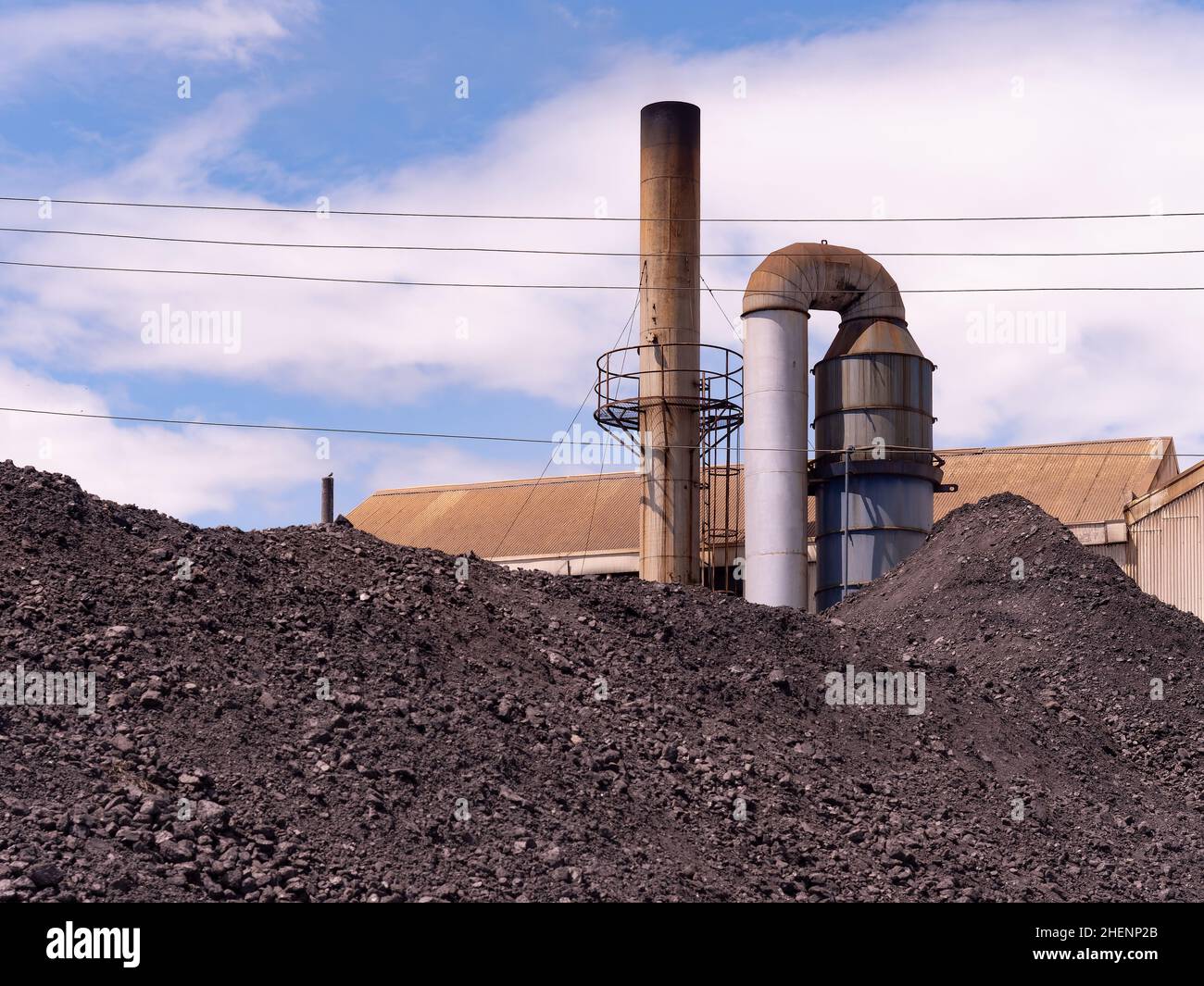 Heaps of coal used to produce steam with boilers at industrial plant. Smoke stack of boiler in the background. Stock Photo