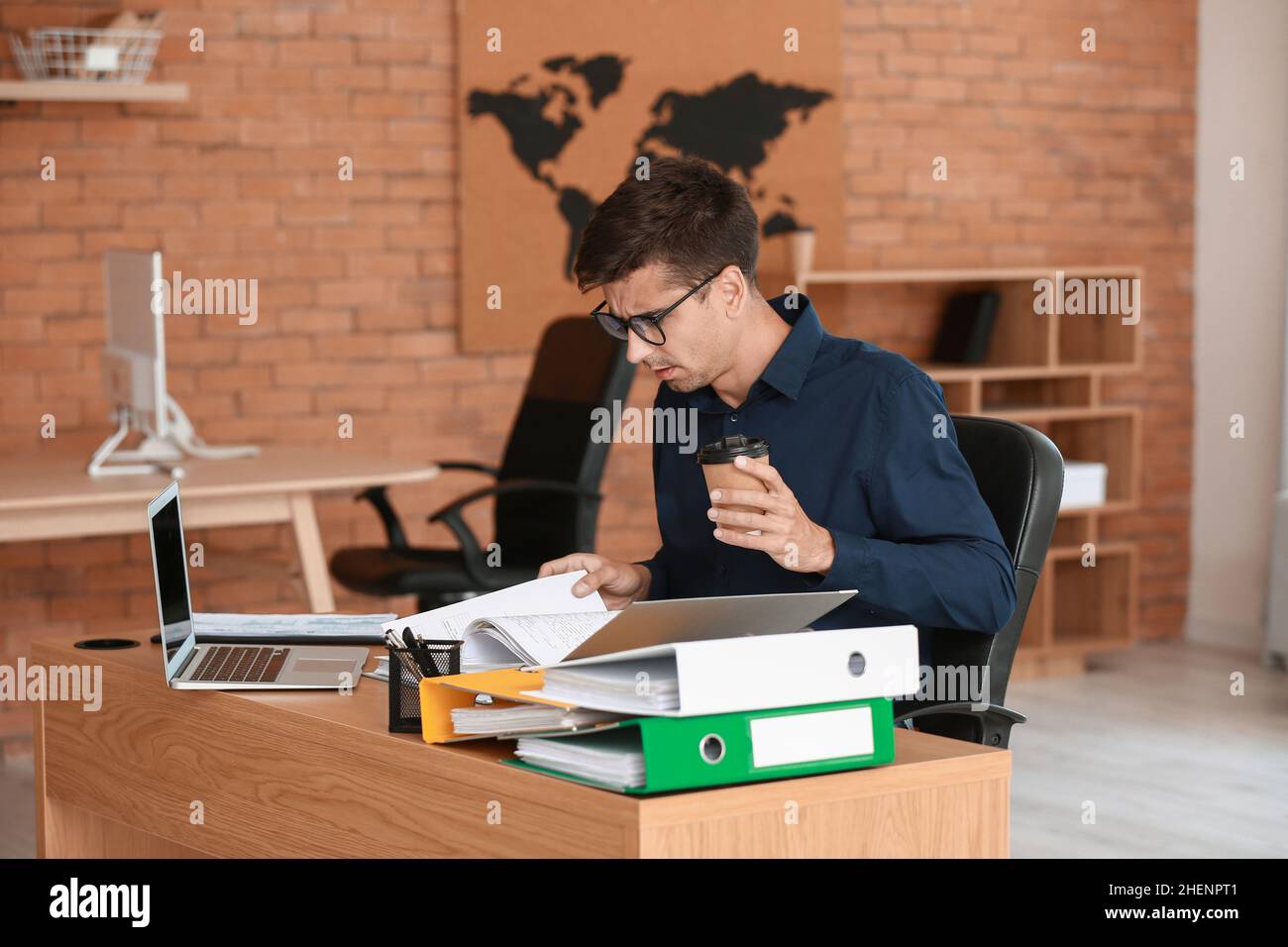 Young man with cup of coffee and open folder at table in office Stock ...