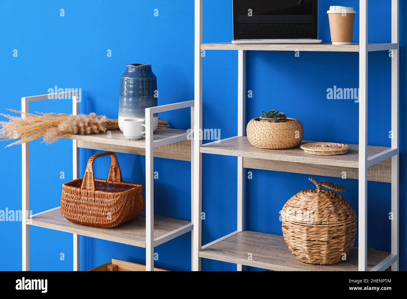 Shelving unit with decor, laptop computer and cups of coffee near blue wall Stock Photo