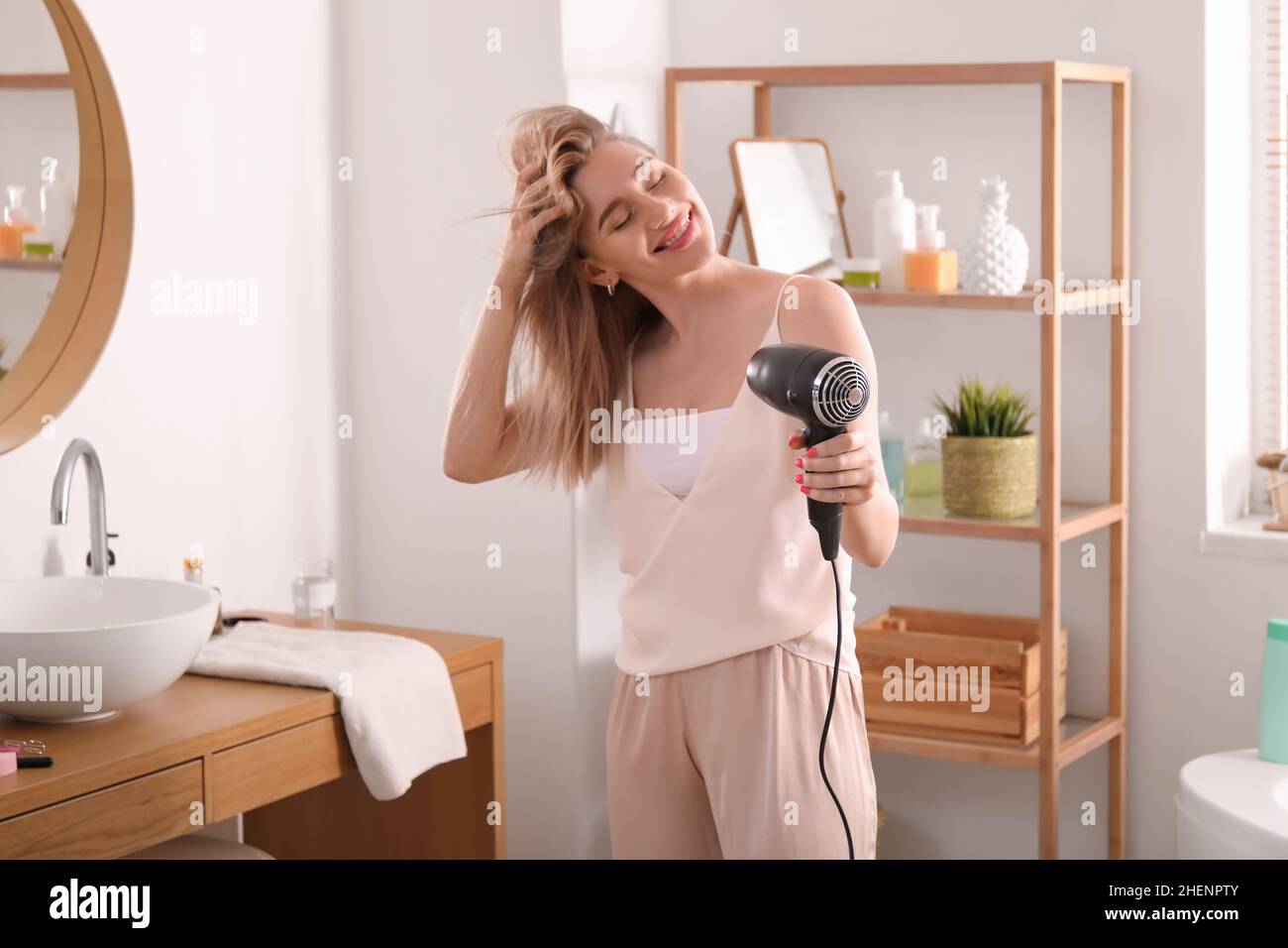 Pretty young woman blow drying her hair in bathroom Stock Photo - Alamy