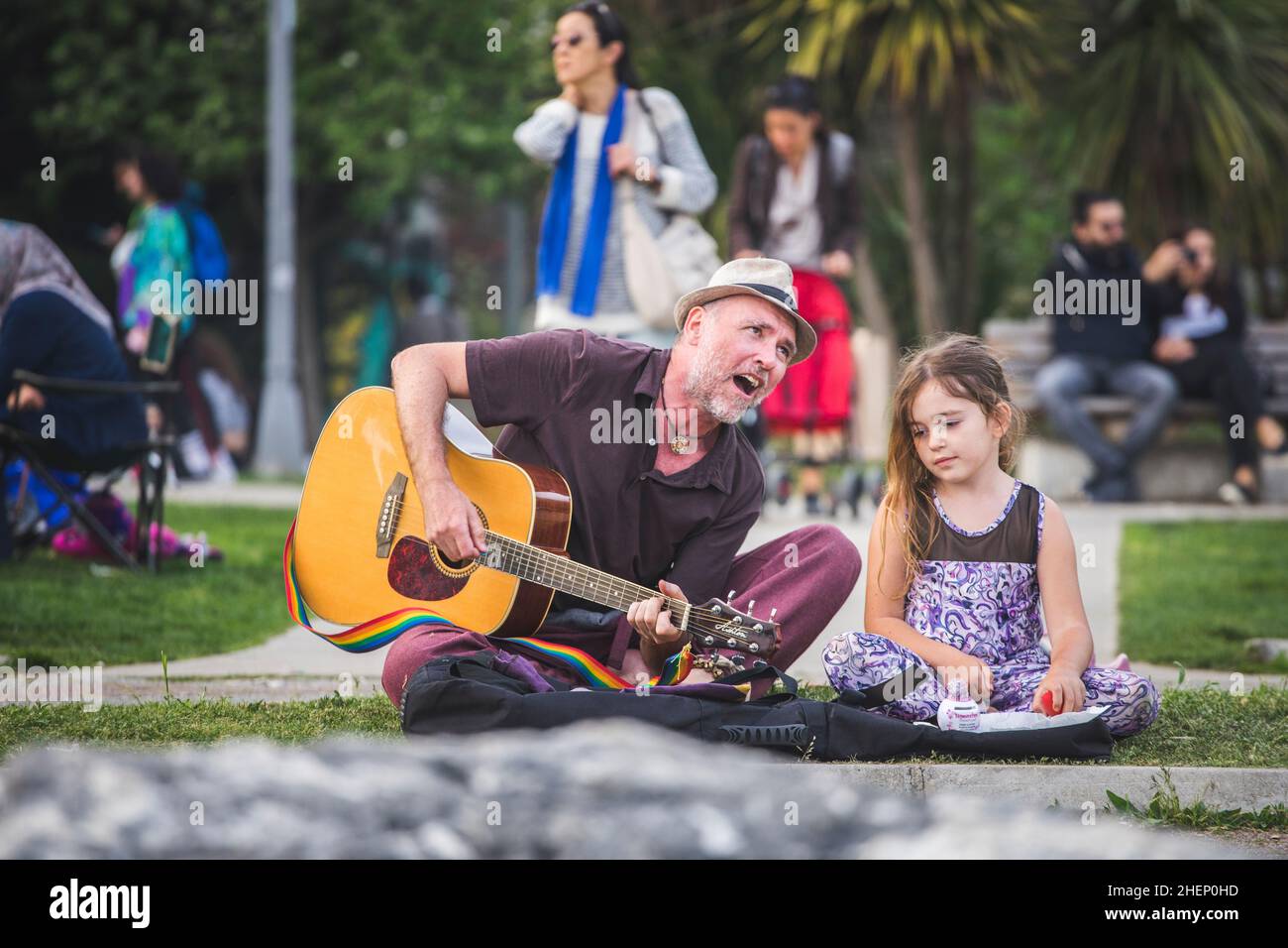 Mature man is playing the guitar and the little girl is listening him on the grass in the park. Stock Photo