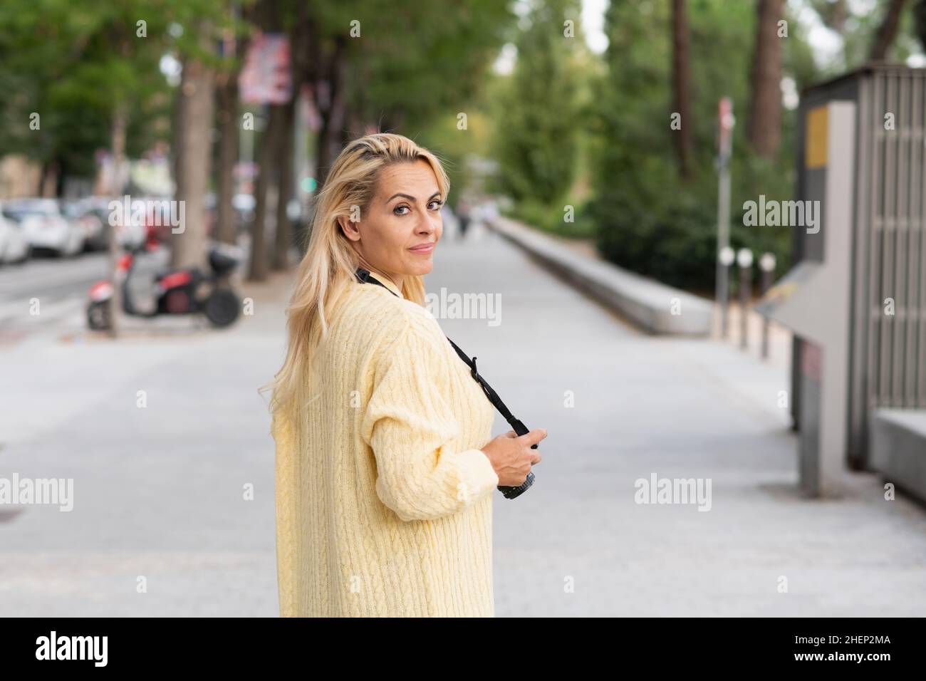 Woman turning to look at the camera while holding a photo camera outdoors Stock Photo