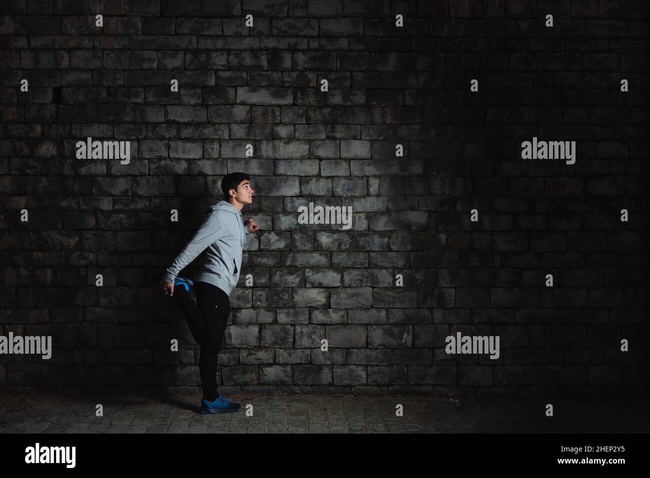 Hispanic teenager sportsman stretching against wall in the darkness. Stock Photo