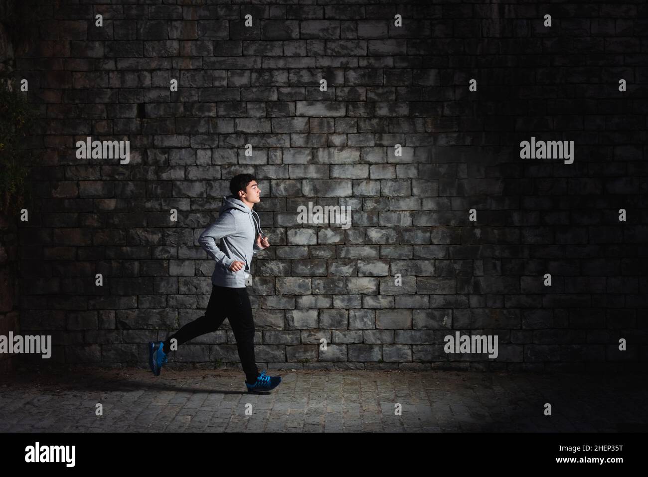 Hispanic teenager sportsman running into the darkness beside a stone wall. Stock Photo