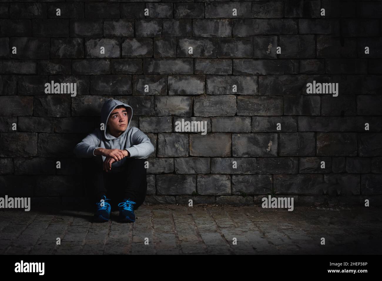 Depressed hispanic teenager sitting against a wall in the darkness. Anxiety and depression in adoloscence concept. Stock Photo