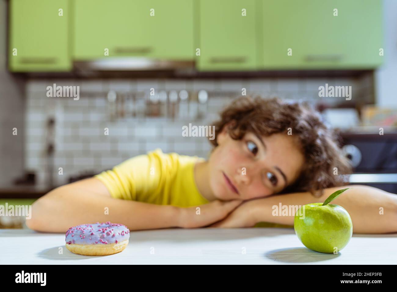 Sad teenage child faced with choice between donut and green apple. tteenage girl with sad face, bruises from malnutrition under her eyes, is on diet Stock Photo