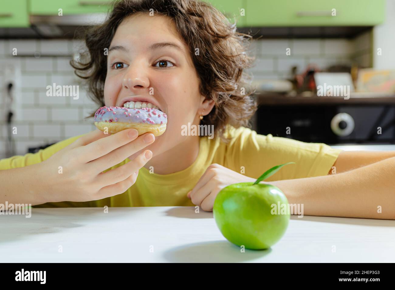 Sad teenage child faced with a choice between donut and green apple. tteenage girl with sad face, bruises from malnutrition under her eyes, is on diet Stock Photo