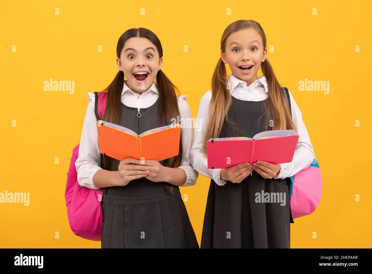 Surprised children in formal uniforms read school books yellow background, library Stock Photo
