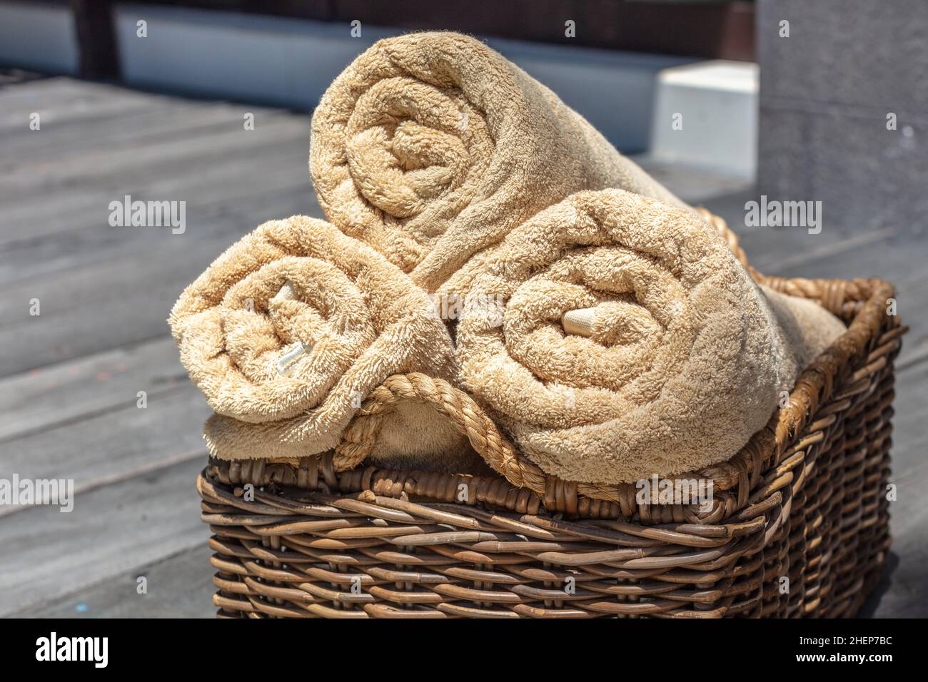 Three rolled beige color towels in a thatched rattan basket. Stock Photo