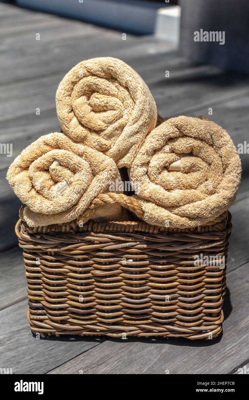 Three rolled beige color towels in a thatched rattan basket. Vertical image. Stock Photo