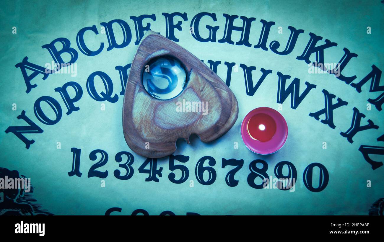 Halloween game with Ouija board. Pointer with magnifying glass and tea red candle on planchette. Scene in haze with smoke. Ghost possesion. Spiritual Stock Photo