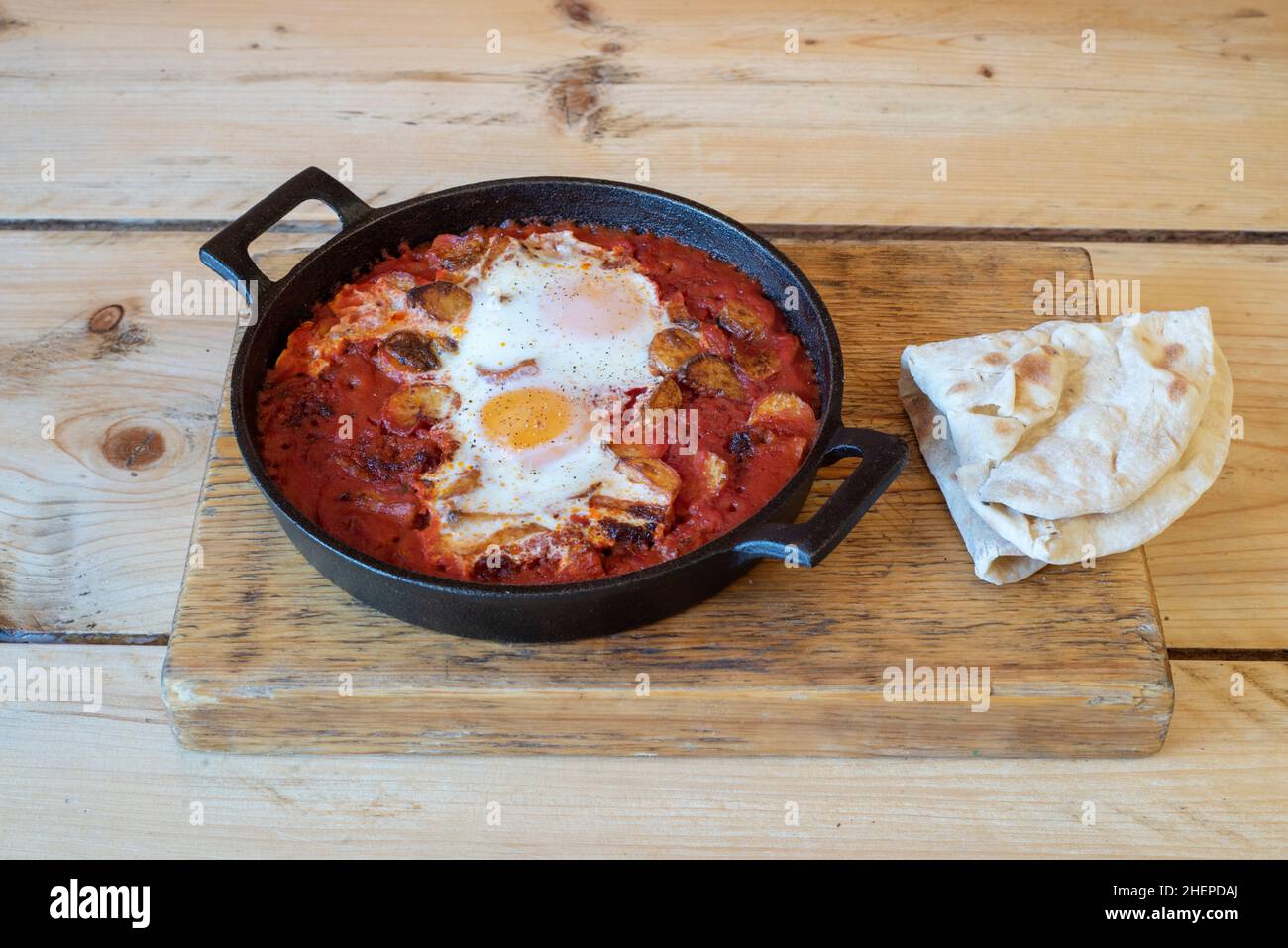 Egg, tomato & mushroom vegetarian breakfast sizzler in tomato sauce with dipping bread served in a hot cast iron skillet Stock Photo