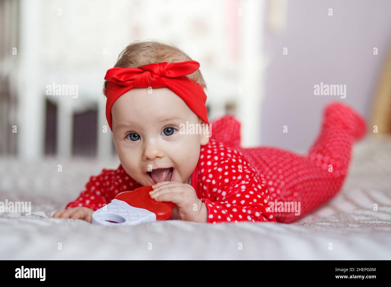 Happy kid lies on bed on stomach. Toddler girl smiling Stock Photo