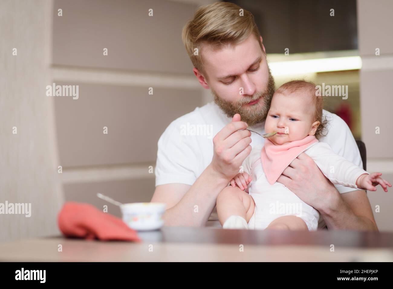 Dad feeds his naughty baby who refuses to eat fruit puree Stock Photo
