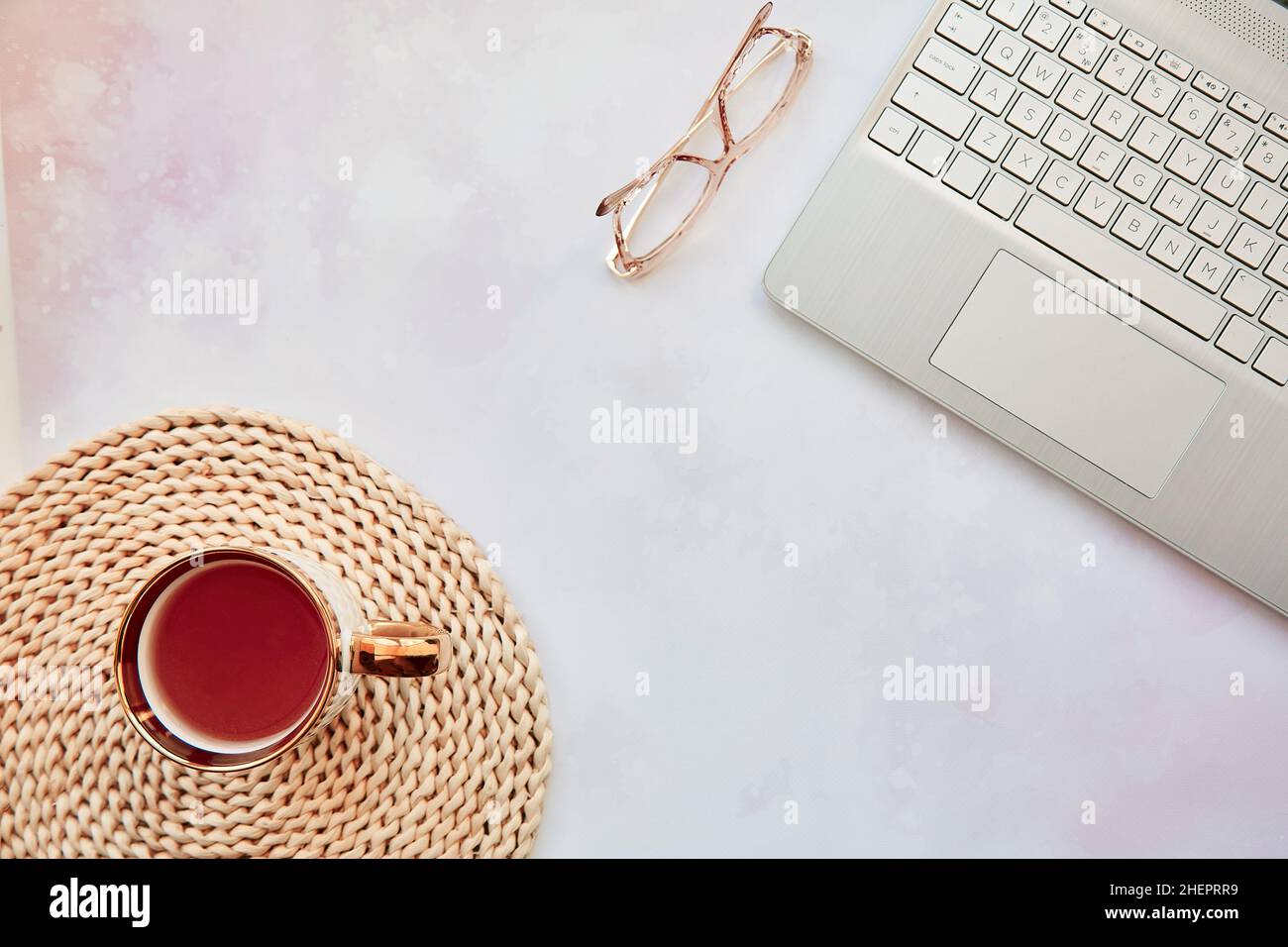 Aesthetic home office: laptop, tea cup and glasses. Feminine concept, remote work, freelance, taking webinar, video calling family because of quarantine concept. Copy space, view from above. Stock Photo