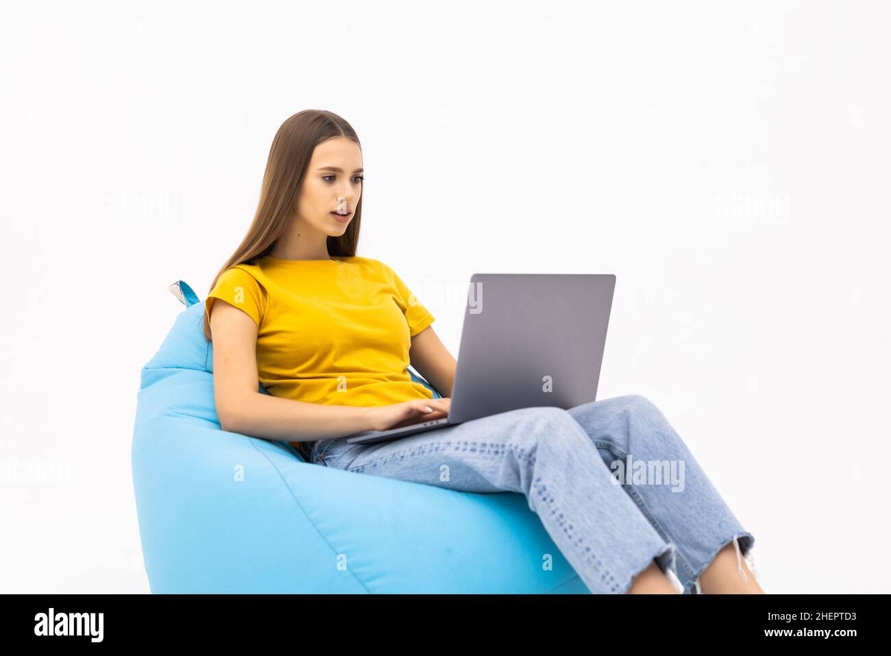 Young female sitting on a bean bag chair and using a laptop isolated on ...
